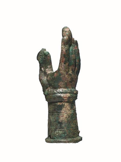 Rimini, Domus del Chirurgo, main votive liée au culte de Iuppiter Dolichenus. Il s'agit d'une sculpture vide en bronze à la cire perdue représentant une main droite ouverte, rendue de manière naturaliste, avec des rainures qui délimitent les ongles et les plis intérieurs des doigts. Un serpent à écailles avec une tête en crête s'enroule autour du poignet et se lève le long du pouce. Dans la partie supérieure, entre l'index et le majeur, il y a un élément ovoïde, semblable à un bourgeon dont la tige est bloquée par les doigts. (Image reproduite avec l'aimable autorisation du Ministero per i Beni e le Attività Culturali - Soprintendenza Archeologia, Belle Arti e Paesaggio per le Province di Ravenna, Forlì-Cesena e Rimini).
