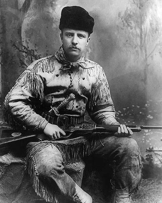 Theodore Roosevelt dans le rôle du chasseur des Badlands. Theodore Roosevelt est en costume de chasse et possède un couteau et un fusil de chasse Tiffany sculptés. Photographié par George Grantham Baine en 1885 à New York. (Domaine public)