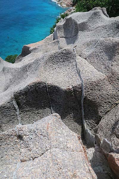 Exemple de roche granitique dans la falaise de Gros la Tête - île d'Aride, Seychelles. Les fines couches plus brillantes sont des veines de quartz, formées lors des derniers stades de cristallisation des magmas granitiques. On les appelle aussi parfois 
